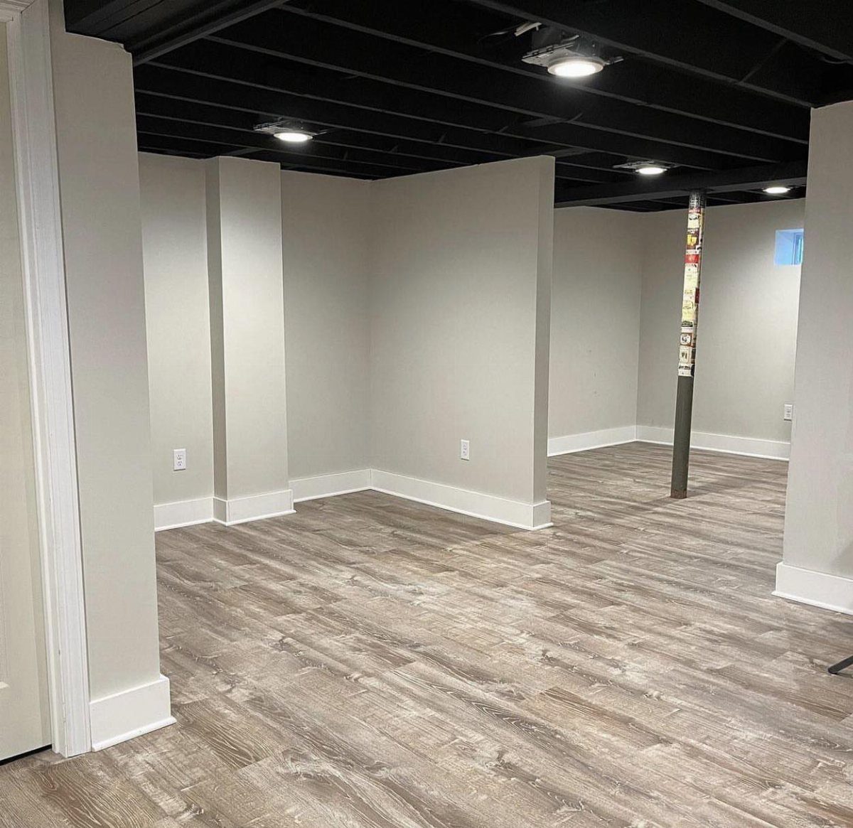 Empty room with black painted open-joist ceiling and light grey walls.