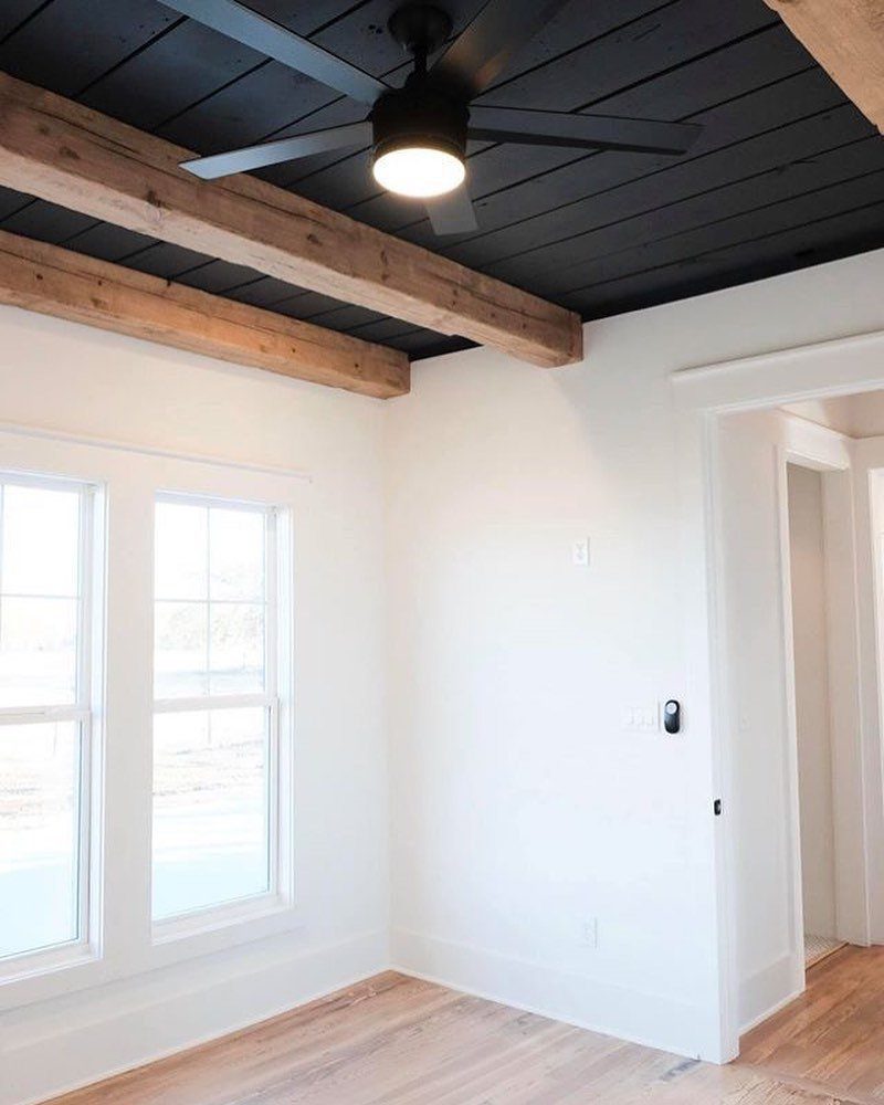 Black shiplap ceiling with natural wood beams and a black ceiling fan.
