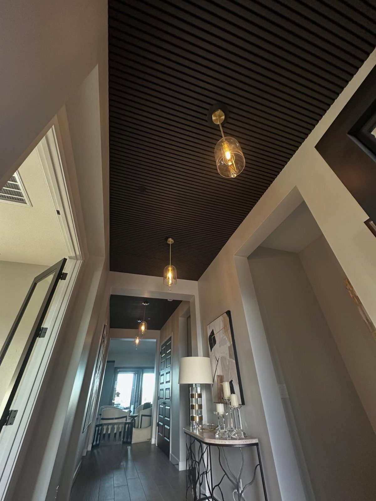 Hallway with black slatted ceiling, grey walls, and gold pendant light fixtures.