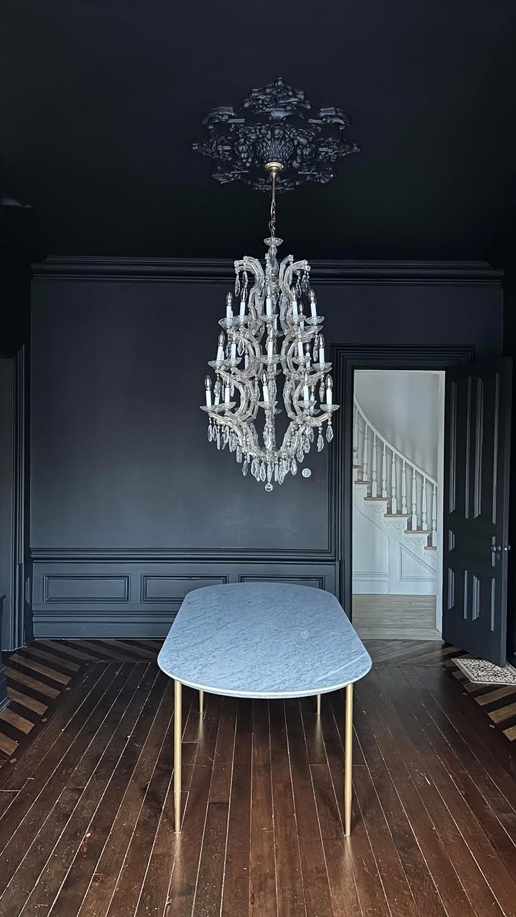 Matte black ceiling in a dark room with a crystal chandelier and white table.