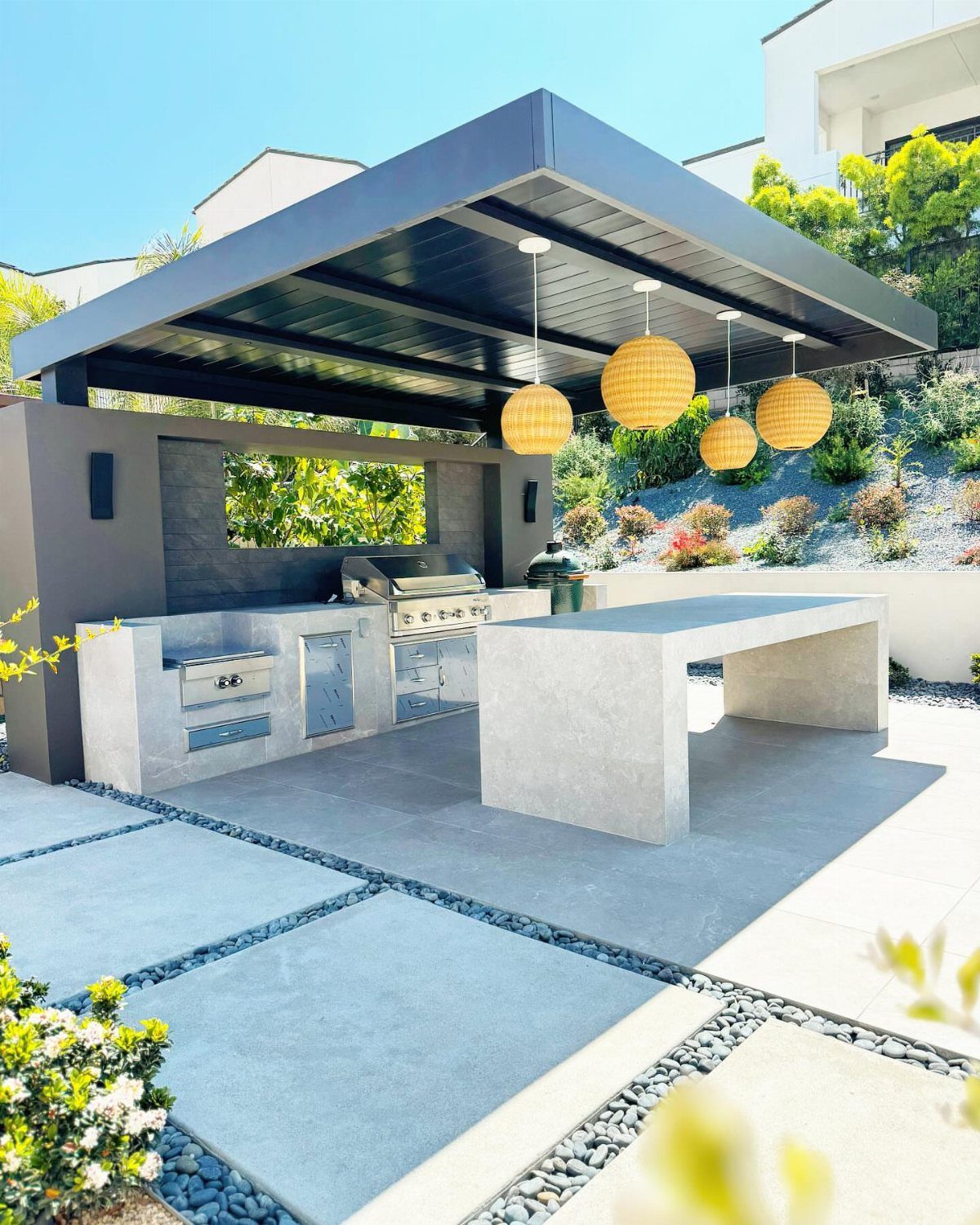 Outdoor kitchen with a black slatted ceiling and yellow spherical pendant lights.