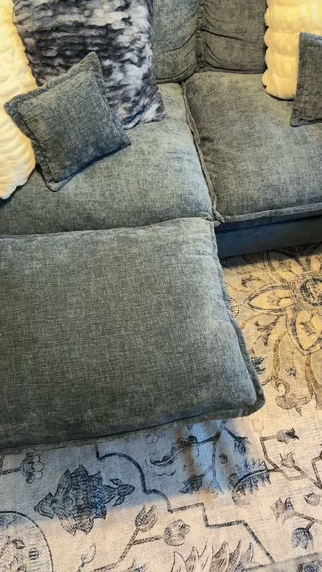 Grey fabric couch with throw pillows sitting on a cream and blue patterned rug