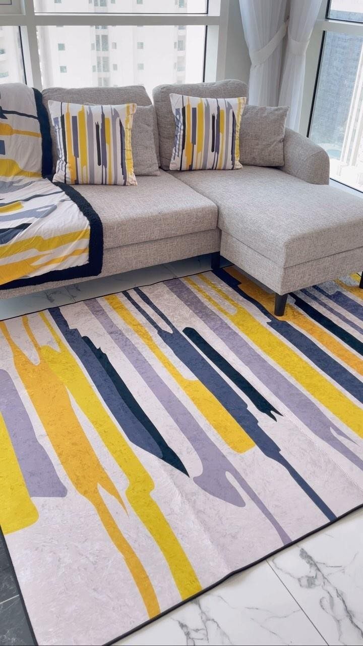 Yellow, grey, and blue abstract rug under a light grey sectional sofa.