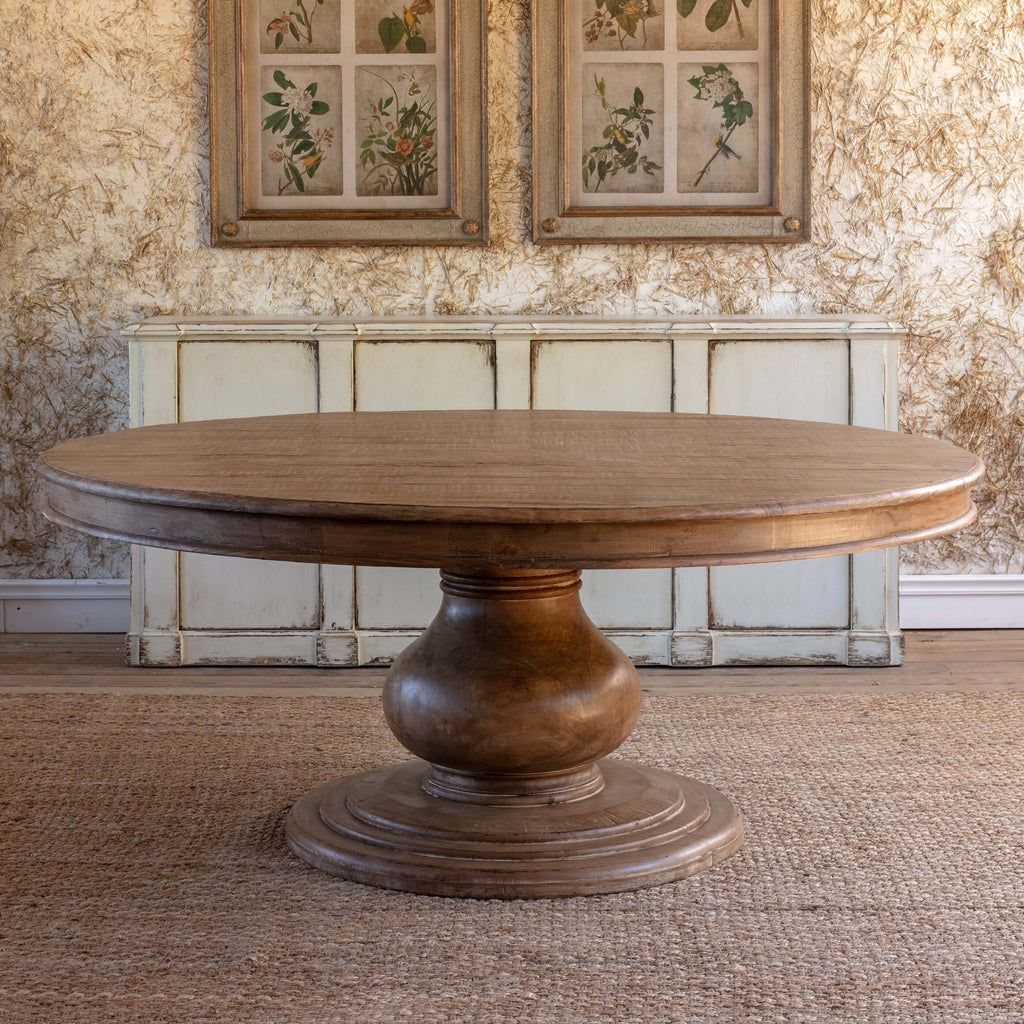 Round wooden coffee table with a carved pedestal base on a woven rug.