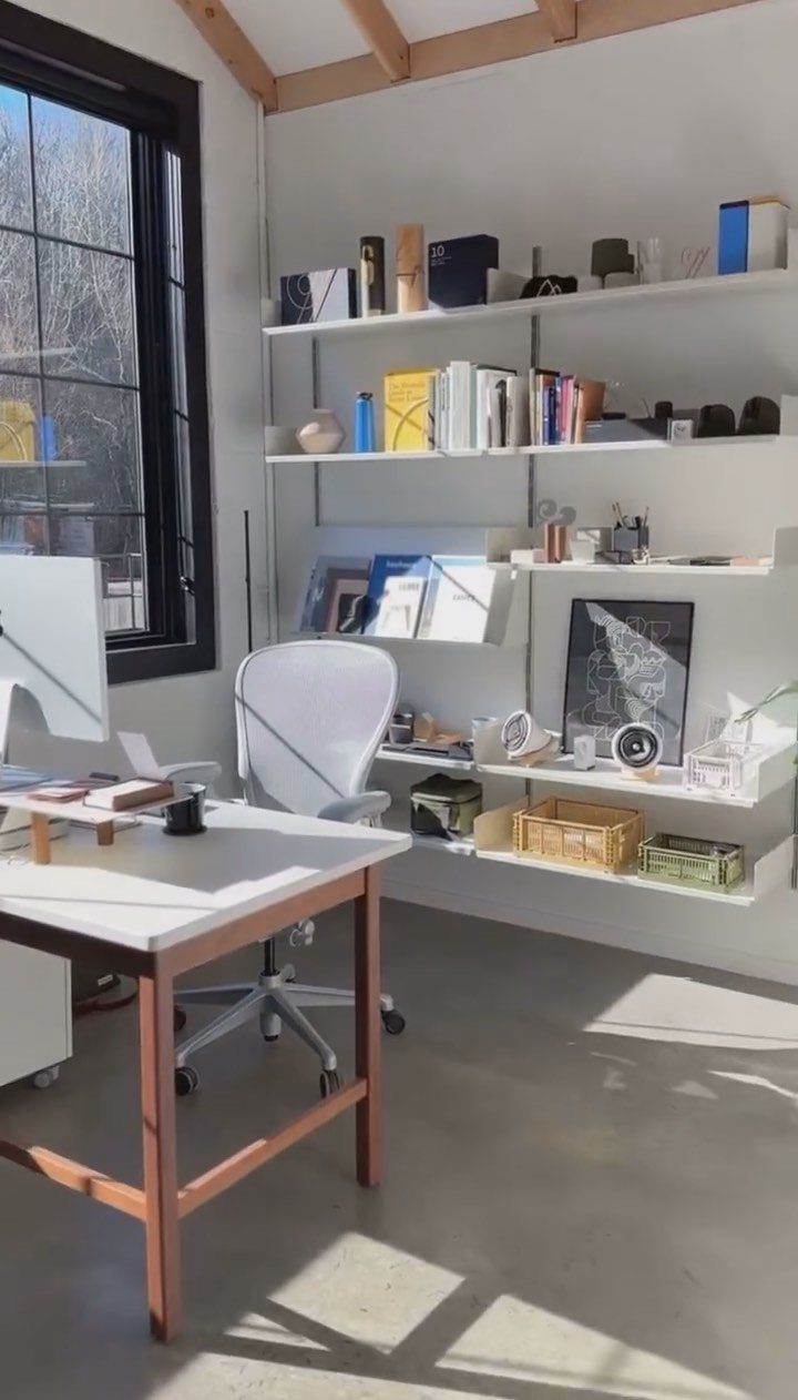 White desk and ergonomic chair in front of organized wall-mounted shelving and window.