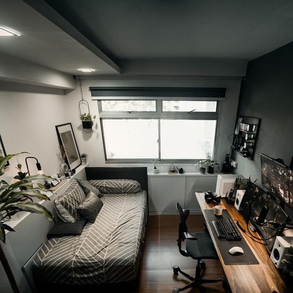 Wooden desk with monitors and a grey striped daybed in a small office.