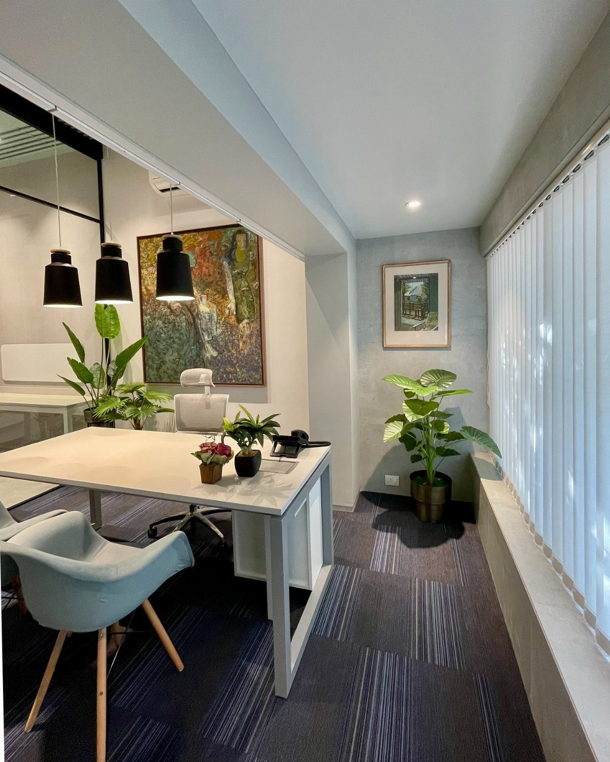 Small office interior with a light desk, blue chair, and potted green plants.