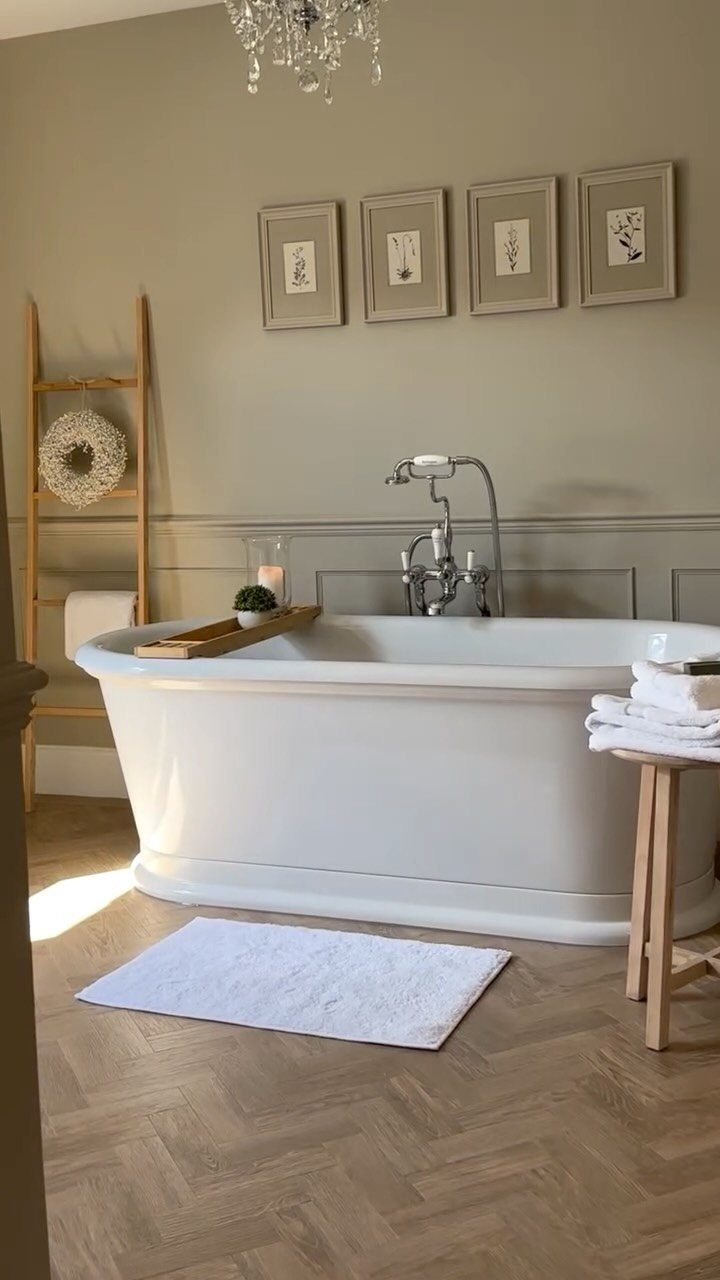 White freestanding bathtub with four framed botanical art prints on the wall above.