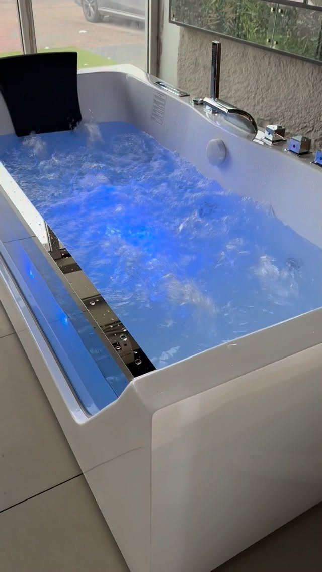 Modern white bathtub with bubbling blue water and chrome fixtures near a window