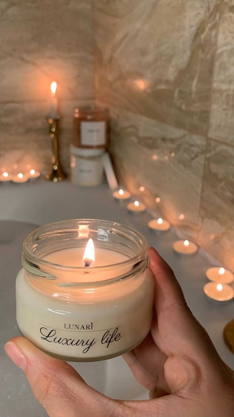 Lit scented candles arranged along the edge of a white bathtub in a bathroom.