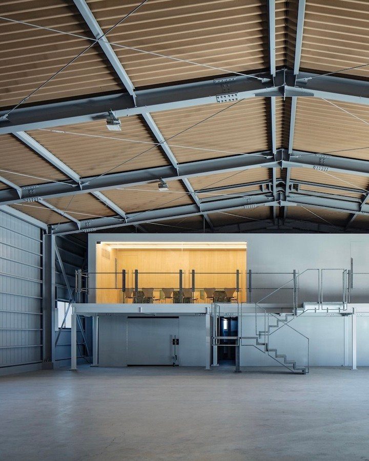 Industrial steel building interior featuring a white mezzanine level and corrugated ceiling.