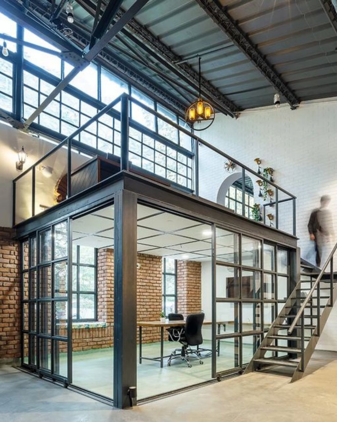 Industrial interior with black steel glass office pod, loft, and exposed brick walls.
