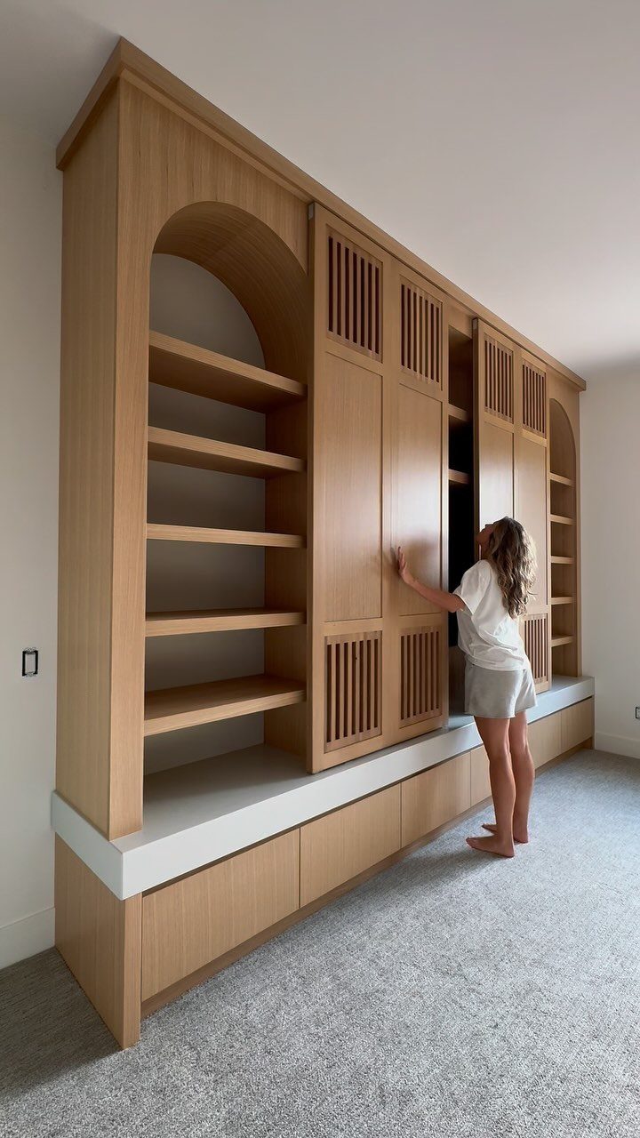 Light wood built-in wall unit with slatted cabinet doors and open arched shelving.