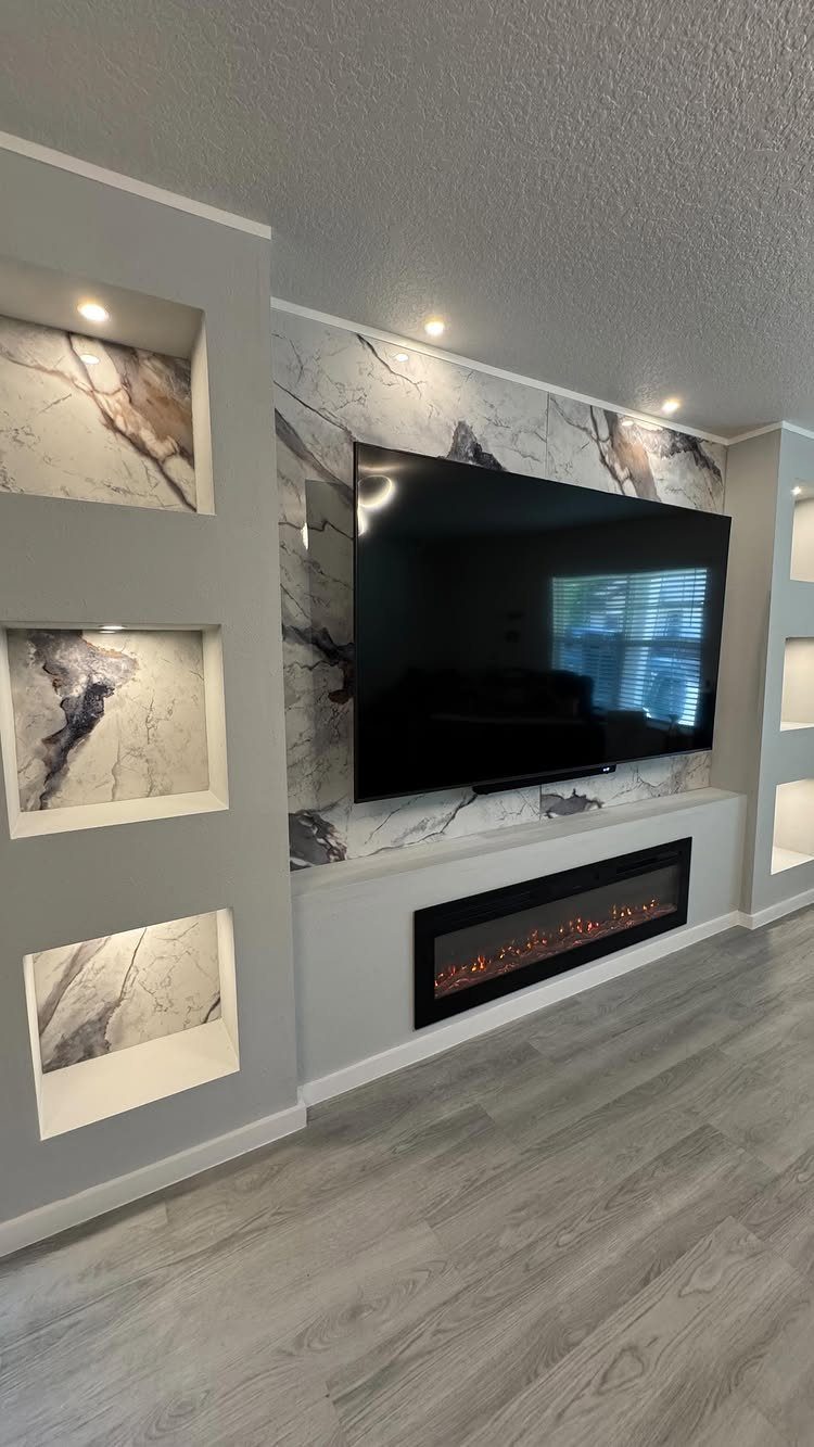 Flat-screen TV mounted on a marble wall above a linear electric fireplace with shelving.