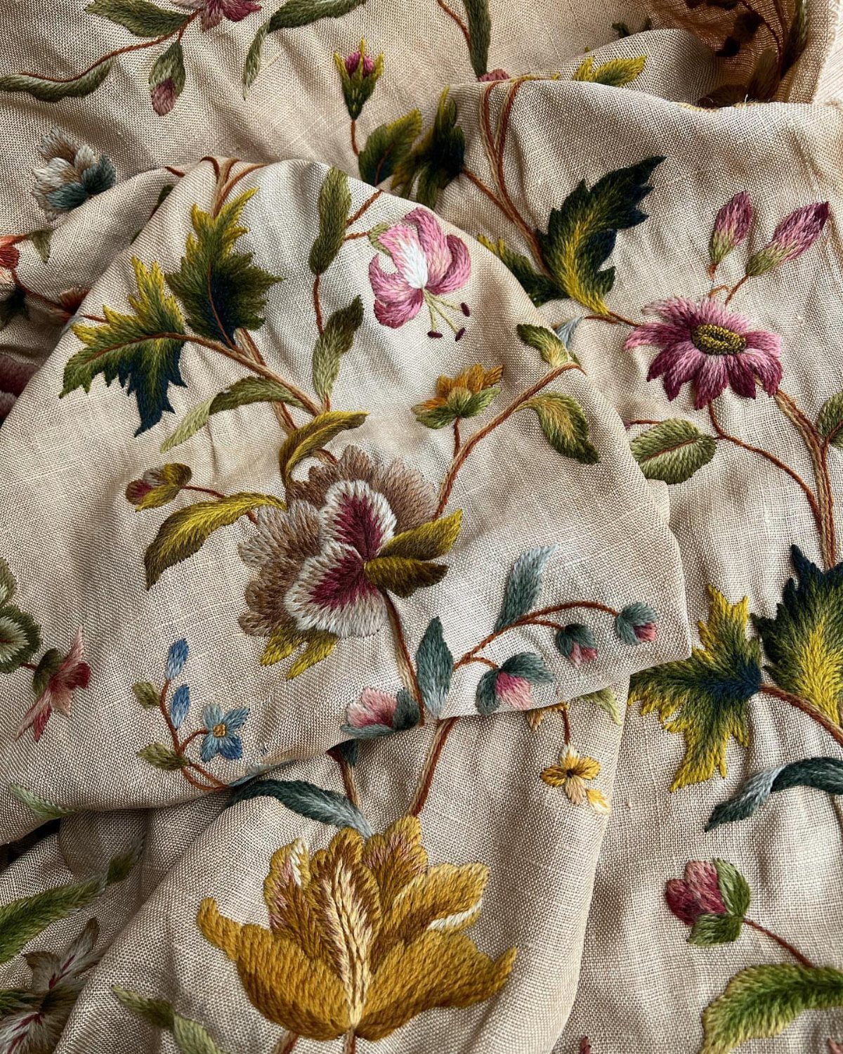 Beige linen fabric with detailed embroidered floral patterns in pink and yellow.
