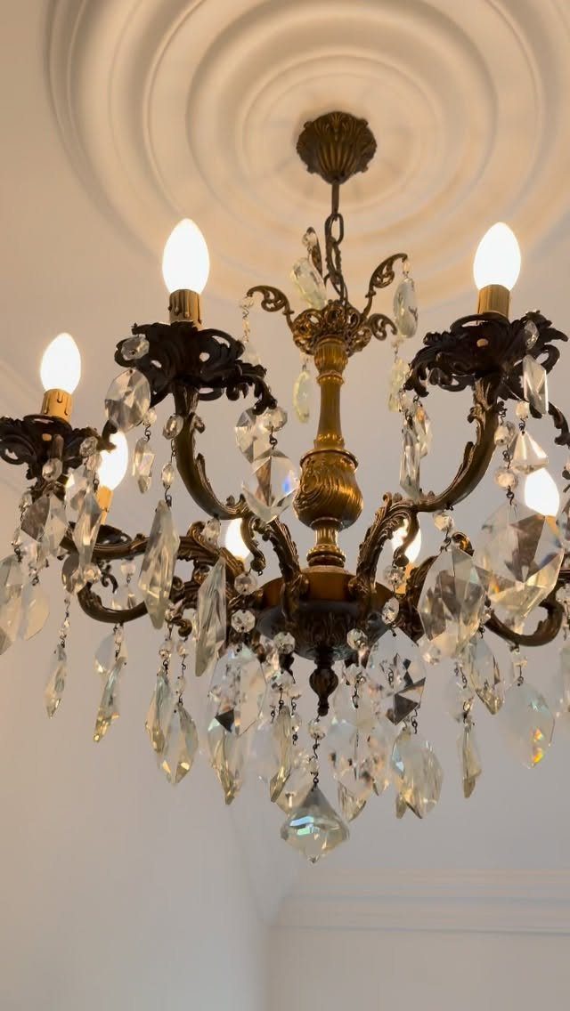 Ornate brass chandelier with hanging glass crystals and lit bulbs on white ceiling