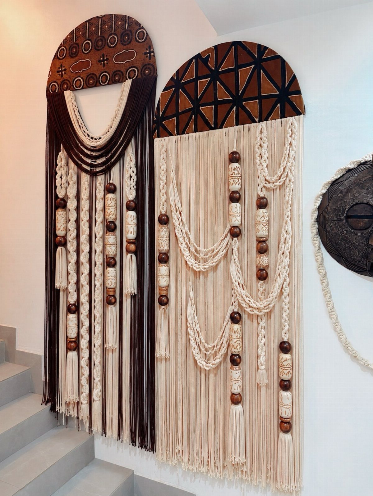 Two large macramé wall hangings with wooden beads on a white wall.