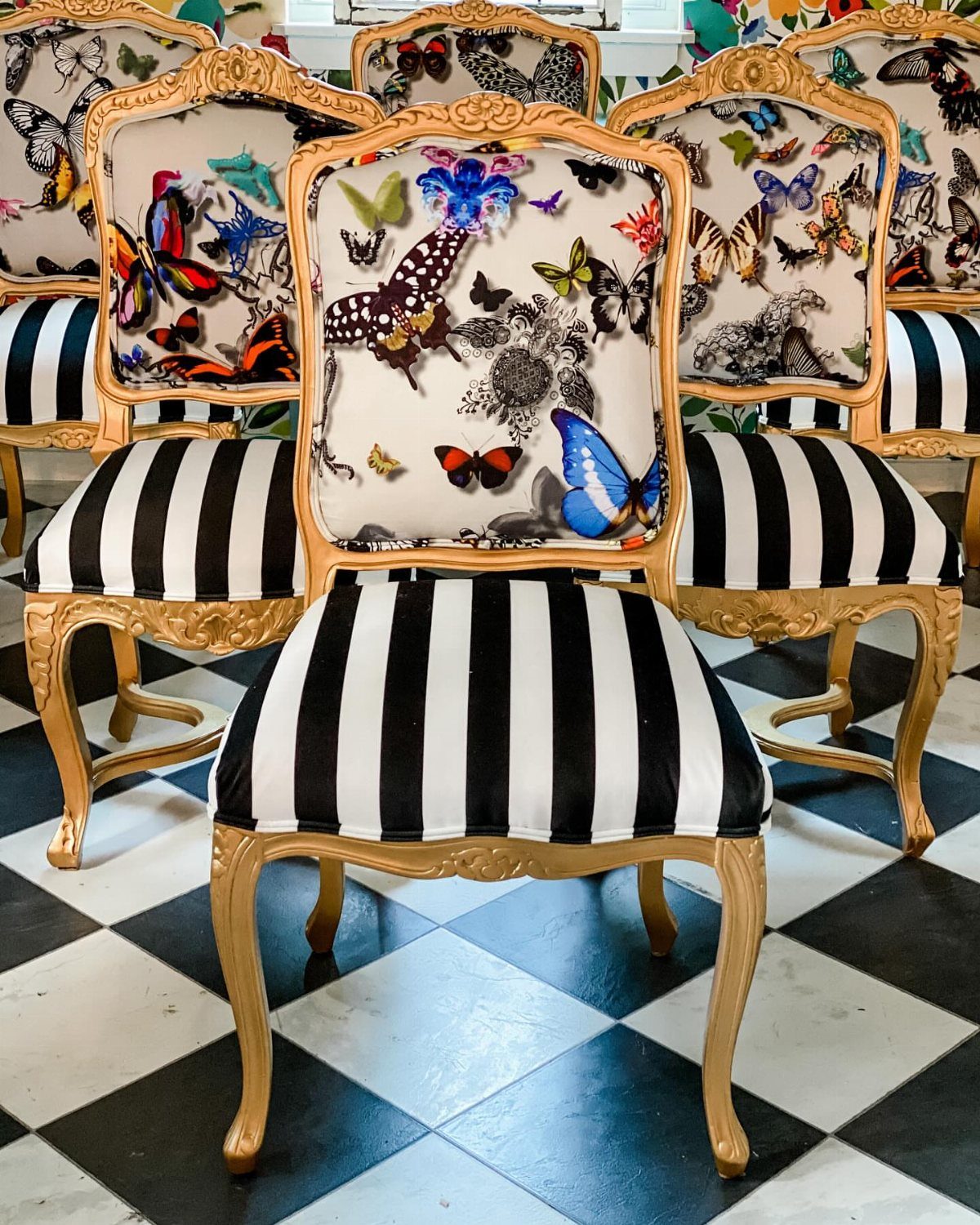 Ornate gold vintage chairs with striped seats and butterfly patterned backrests on checkered flooring