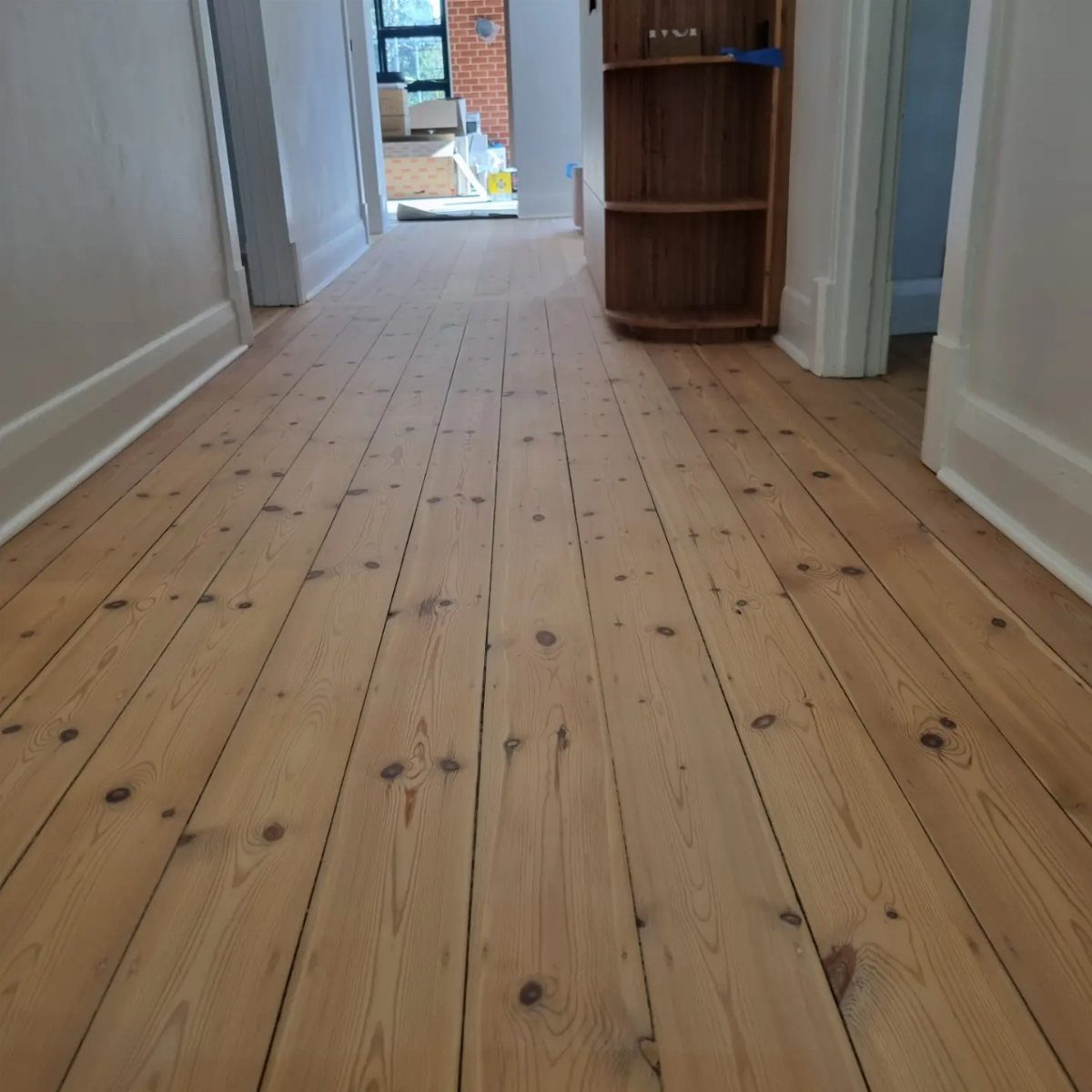 Wide-plank light wood flooring with knots in a bright white hallway