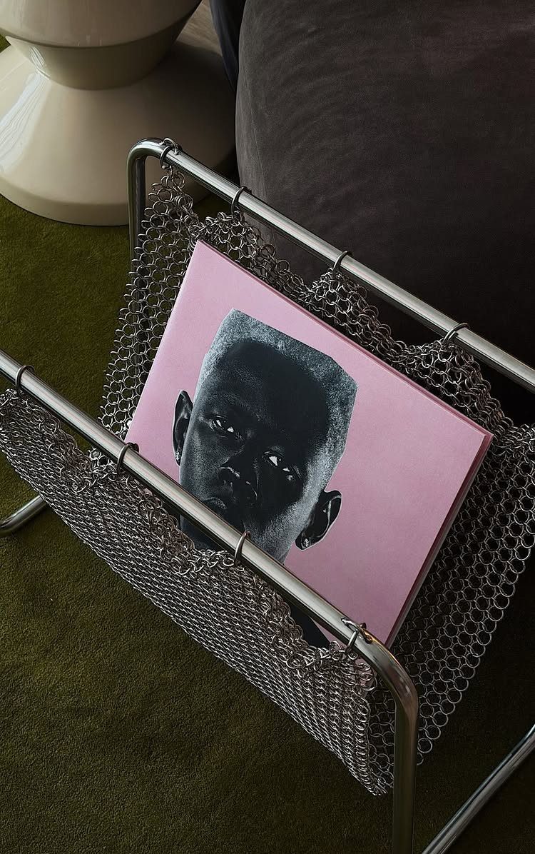 Chrome mesh magazine rack holding a pink book on a green carpet.