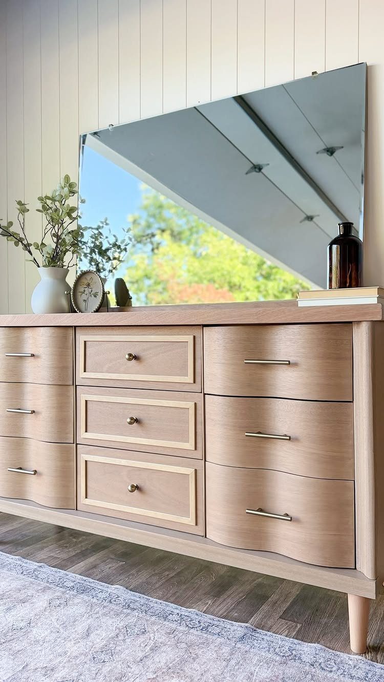 Light wood mid-century modern dresser with tapered legs and a large angled mirror.