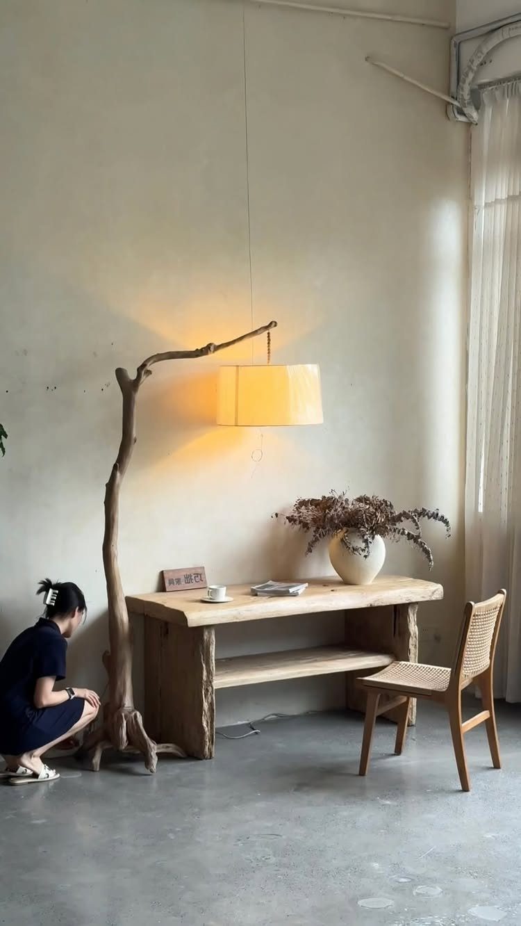 Rustic branch floor lamp illuminating a wooden desk in a minimalist wabi sabi room