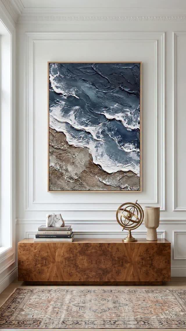 Textured ocean wave painting above a low wooden console in a white room.