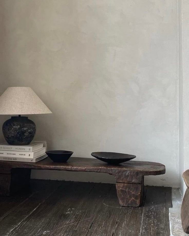 Rustic wooden bench with organic bowls and a ceramic lamp against a textured wall