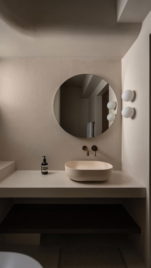 Minimalist bathroom with a round mirror, beige vessel sink, and spherical wall lighting.