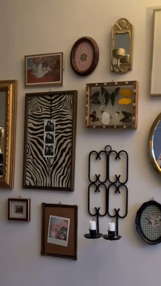 Eclectic gallery wall with framed art, mirrors, and a butterfly display on white wall
