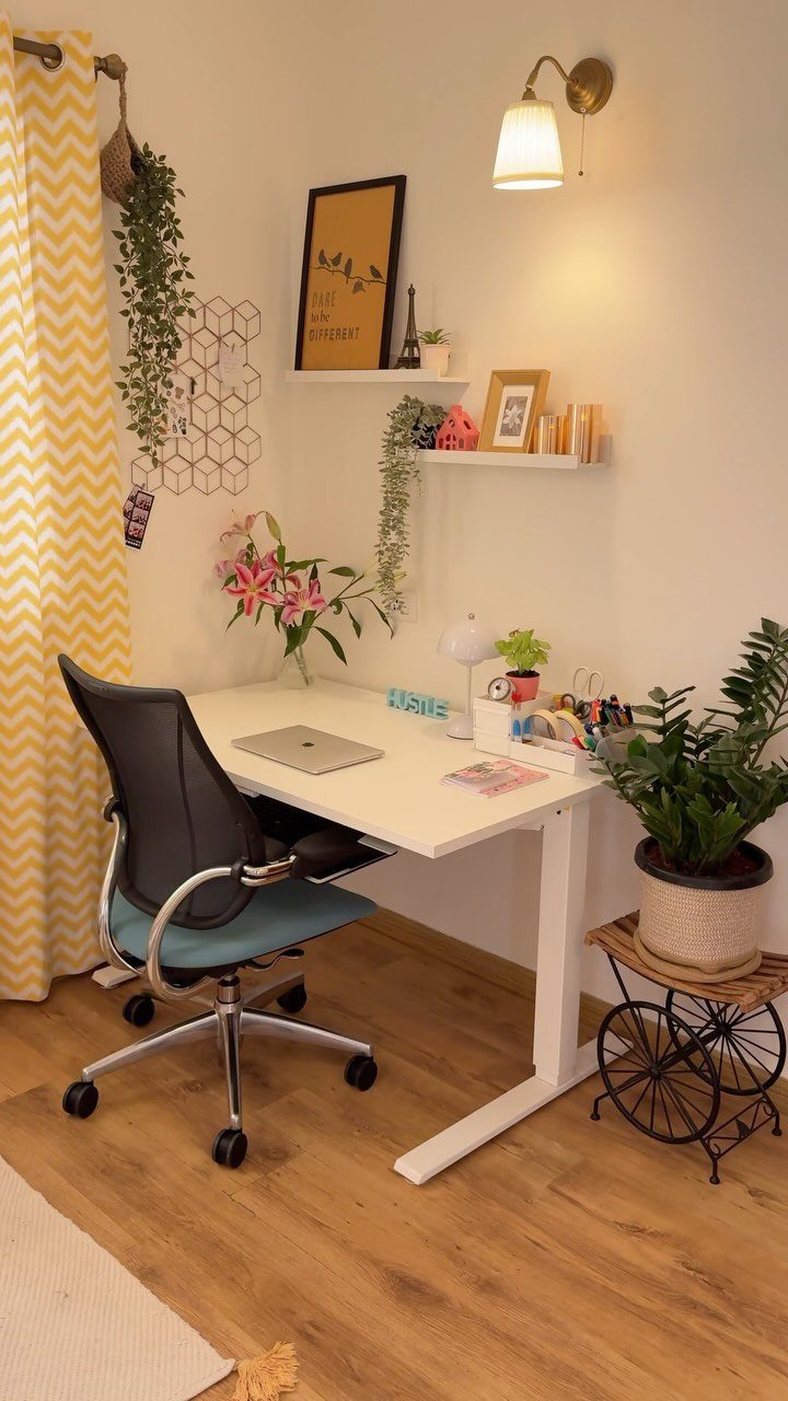 Small white corner desk with a black office chair and surrounding indoor plants.