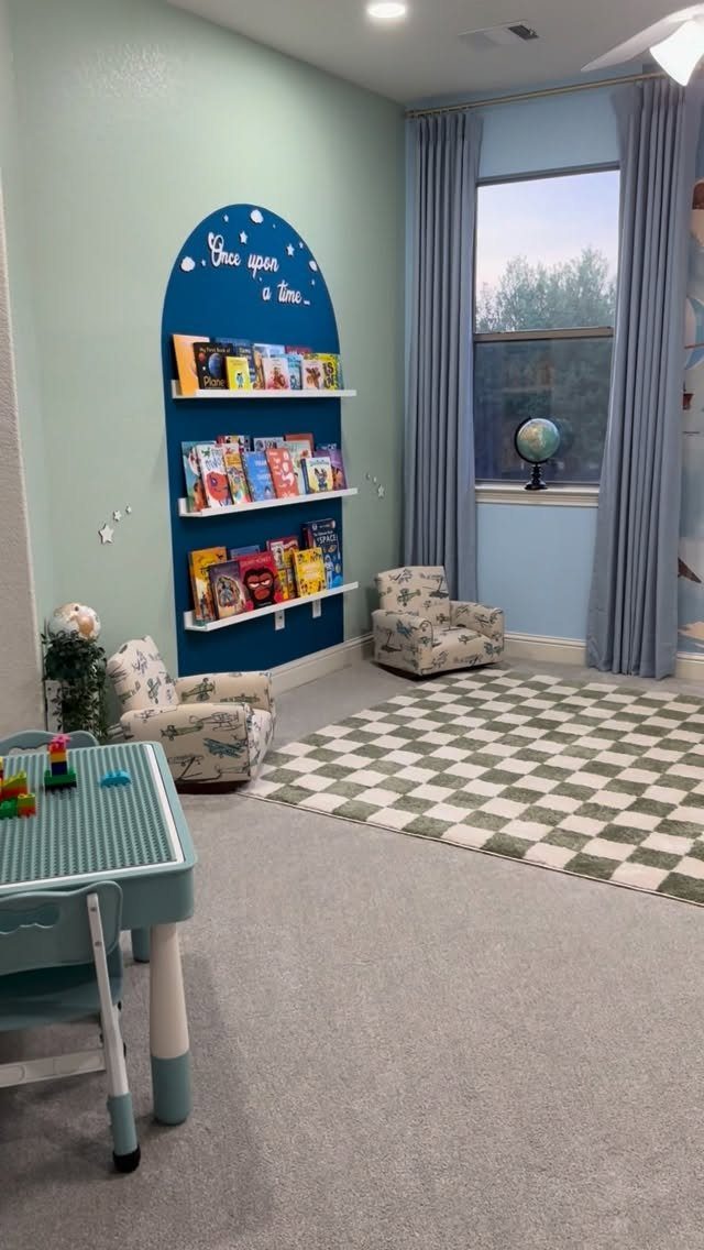 Children's reading nook with blue arched wall, book shelves, and patterned armchairs.
