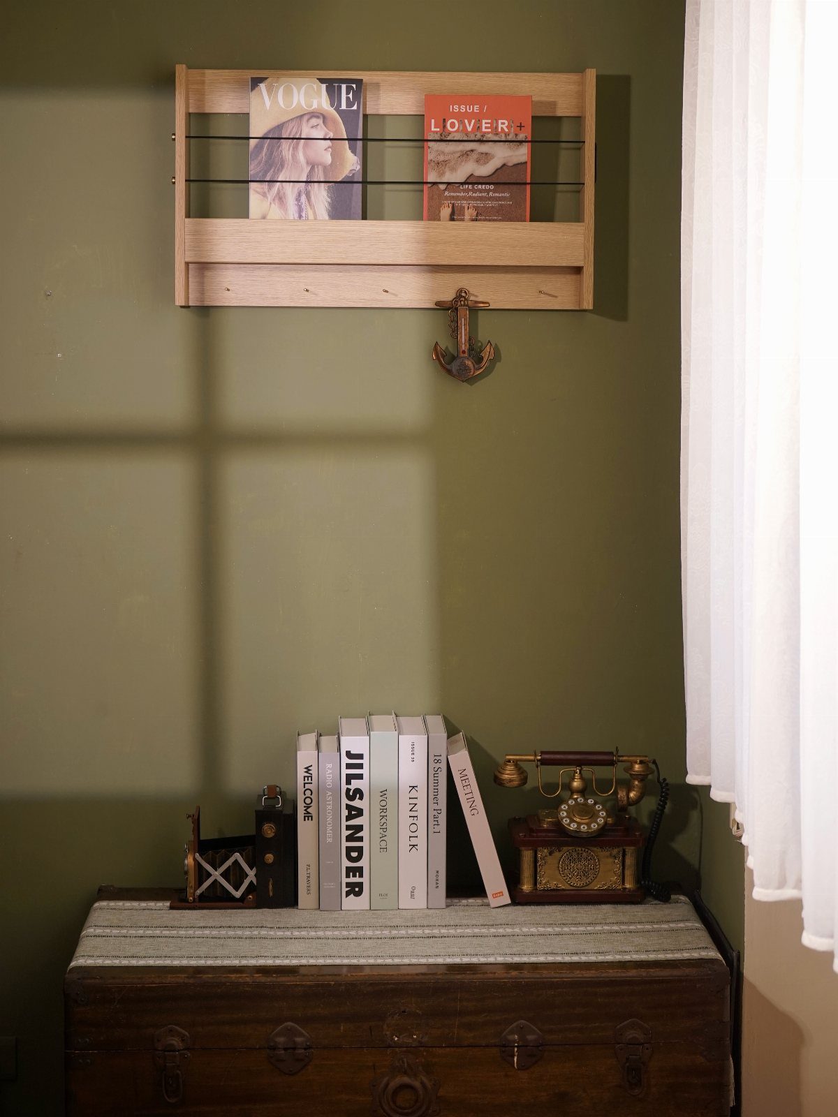 Vintage wooden trunk with books and a rotary phone against a green wall.