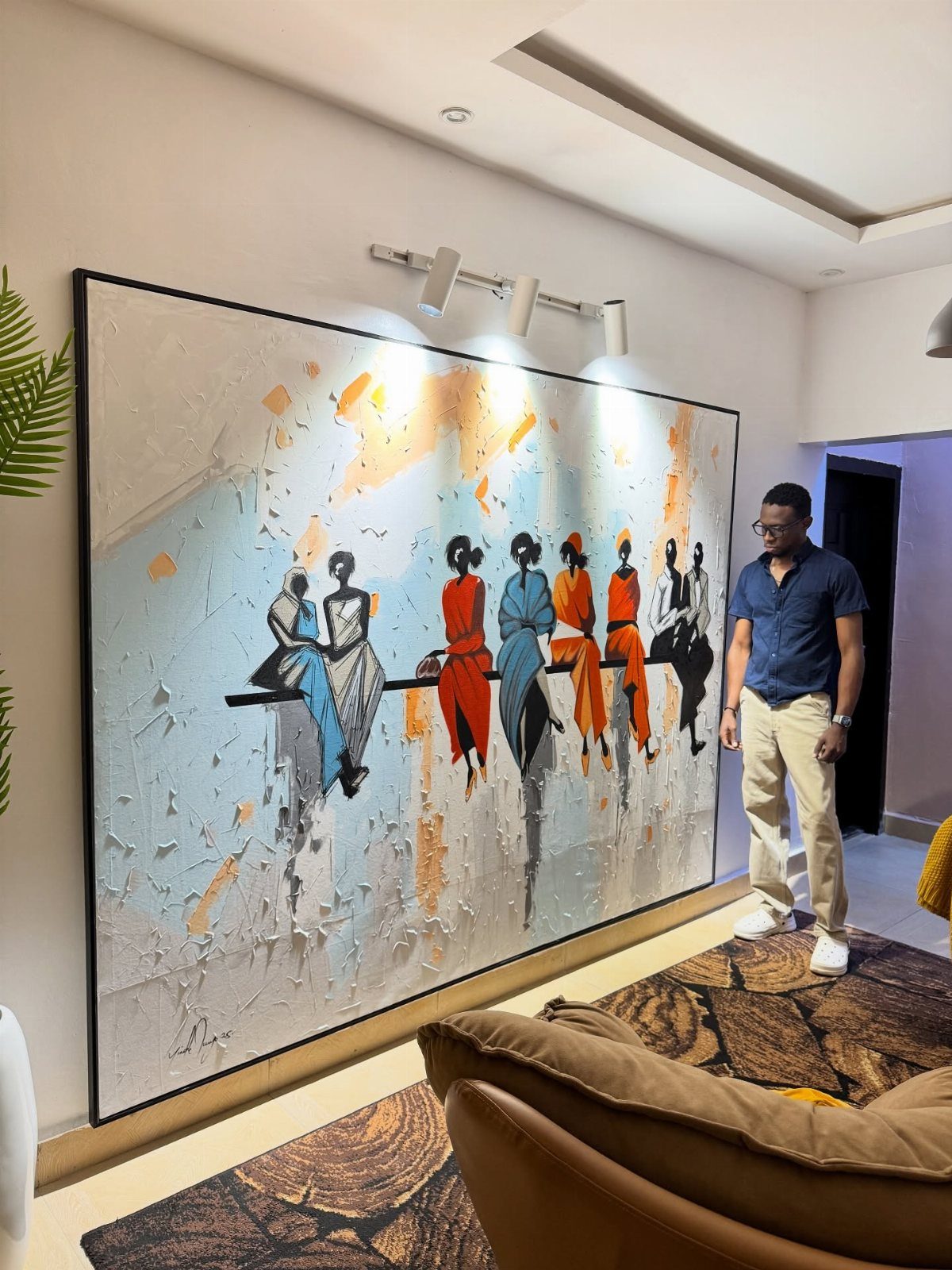 Large textured painting of figures on a white wall above a brown couch