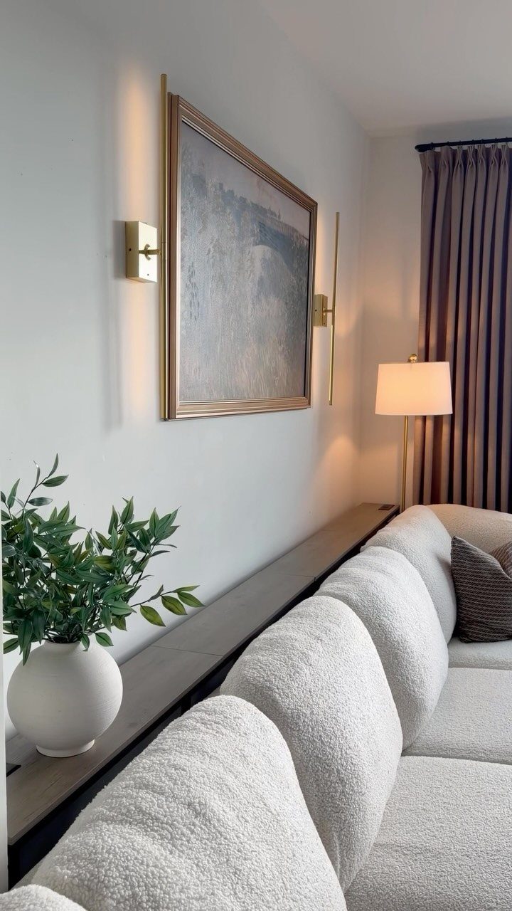 Gold wall sconces flanking a framed painting above a white textured sofa