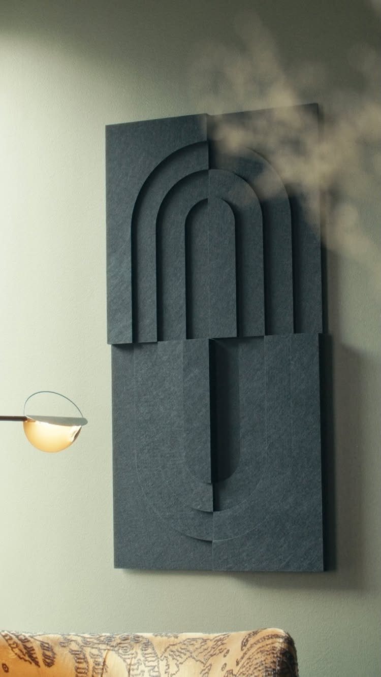 Dark grey sculptural wall art with geometric arches on a sage green wall.