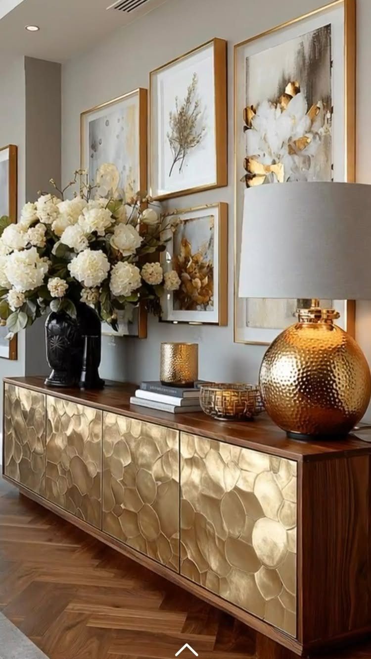 Hammered gold sideboard with a gold lamp and gold-framed art in neutral room.