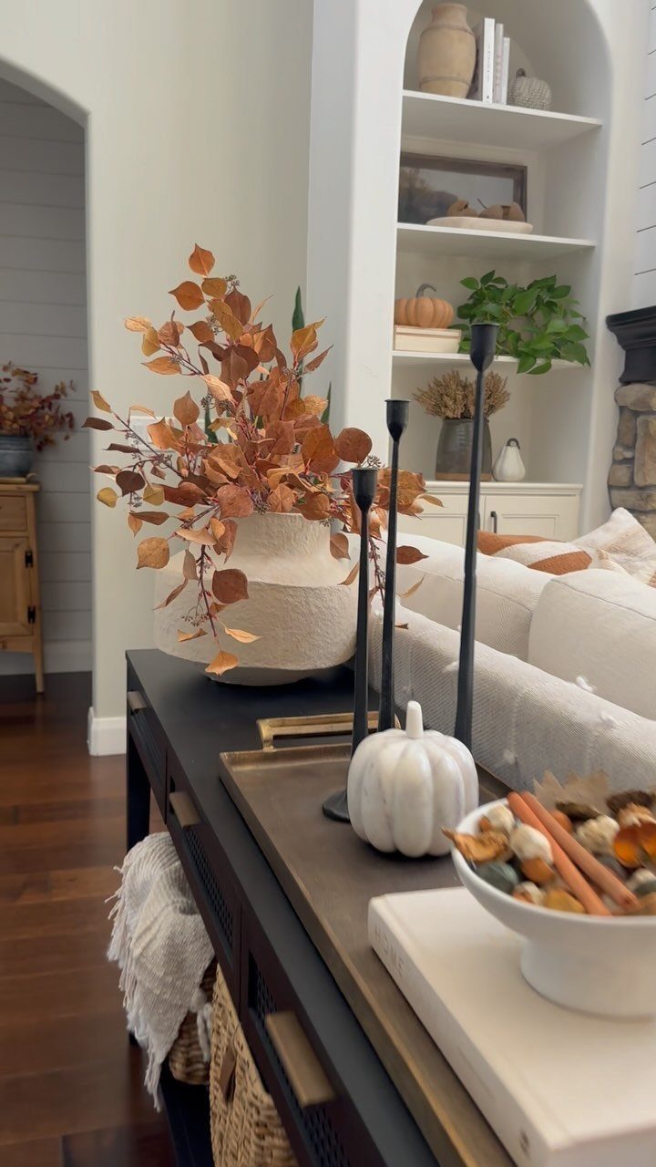 Autumnal home decor on a black console table with white pumpkins and orange leaves.