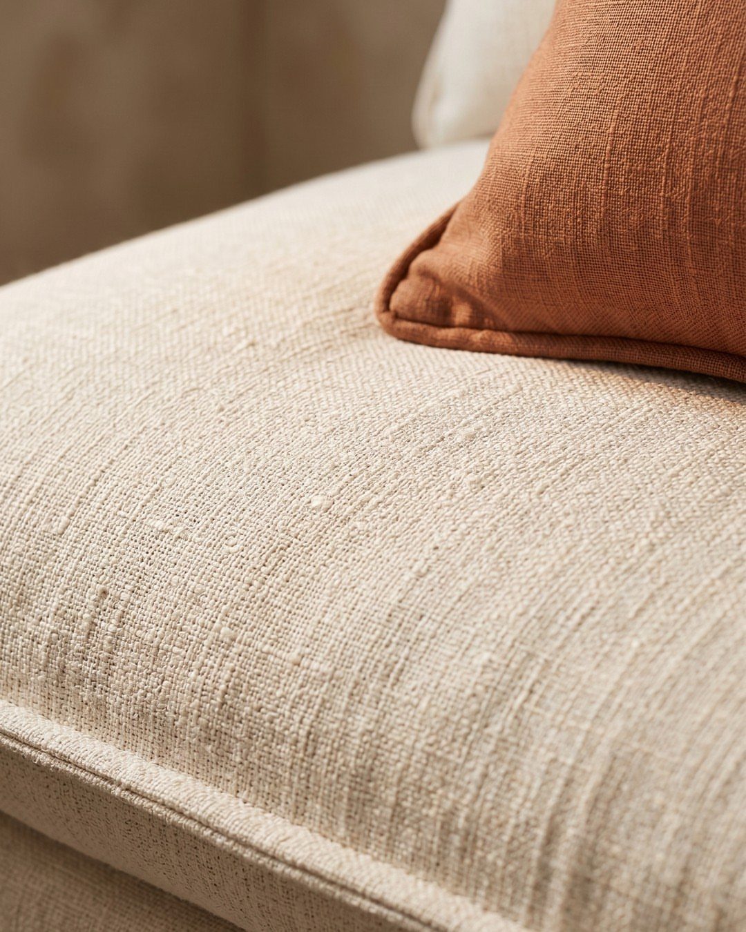 Cream woven sofa cushion with a rust-orange textured pillow resting on top.
