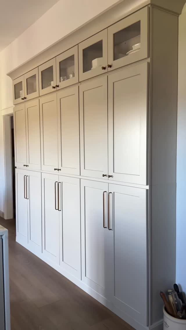 Light grey Shaker-style kitchen cabinets with metallic handles and glass-fronted upper cupboards.